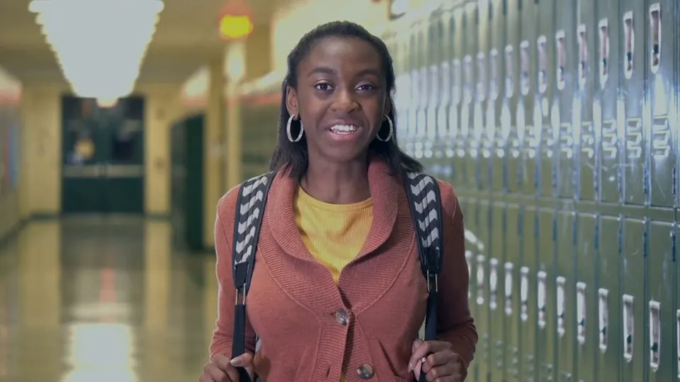 A smiling student with a backpack in a school corridor